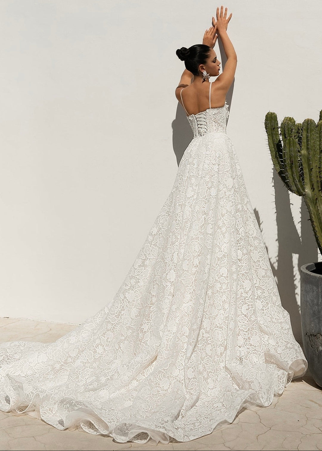 Aeris gown with all over lace and 3D flowers, shown on a petite model in a front view against a rendered wall.
