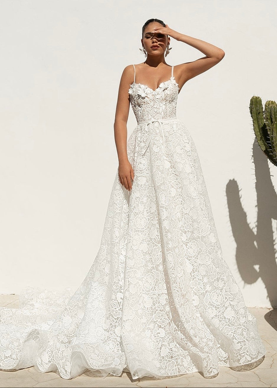 Aeris gown with all over lace and 3D flowers, shown on a petite model in a front view against a rendered wall.
