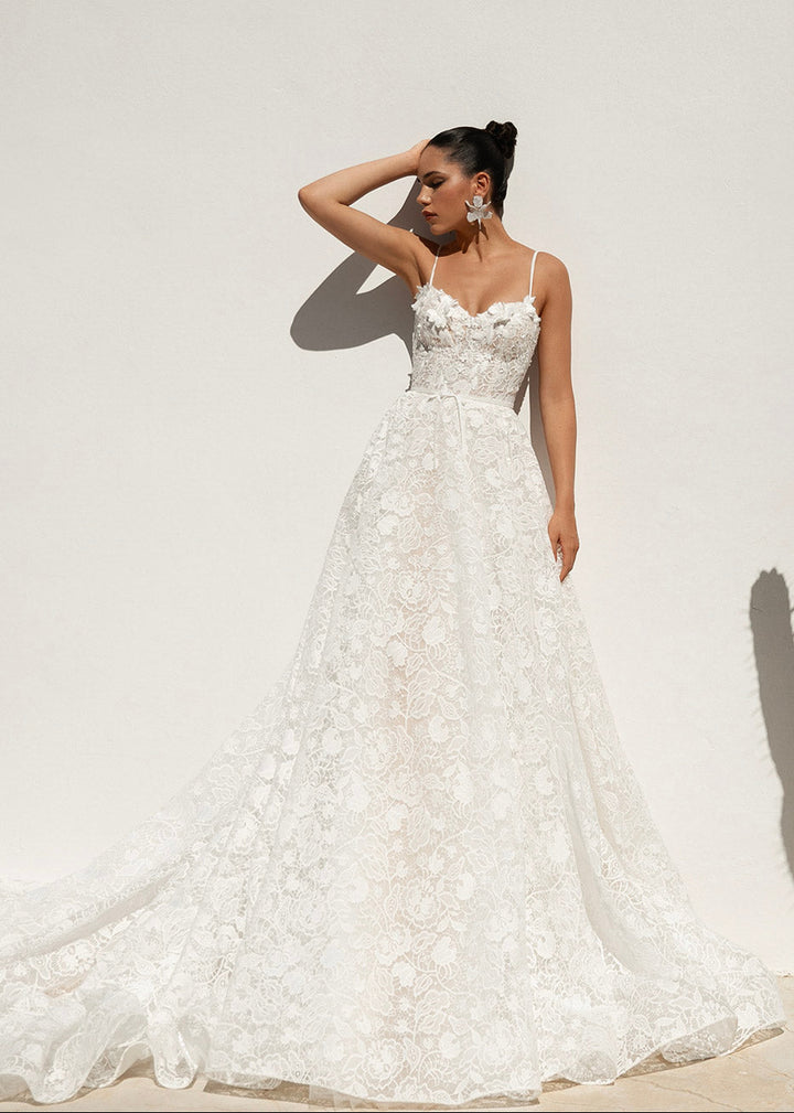 Aeris gown with all over lace and 3D flowers, shown on a petite model in a front view against a rendered wall.
