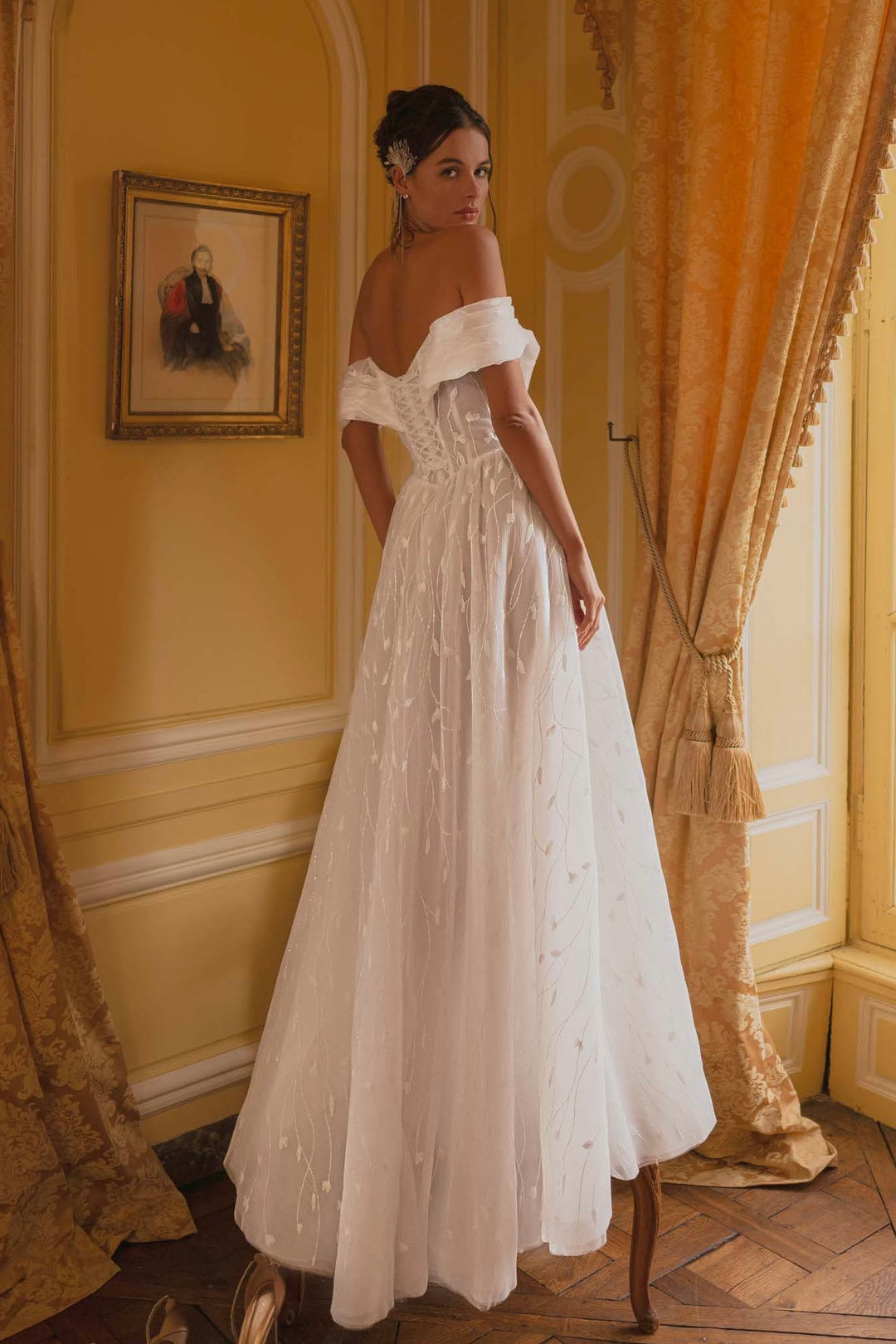 Woman in an off-the-shoulder pleated botanical tulle A-line wedding dress with a lace up back.
