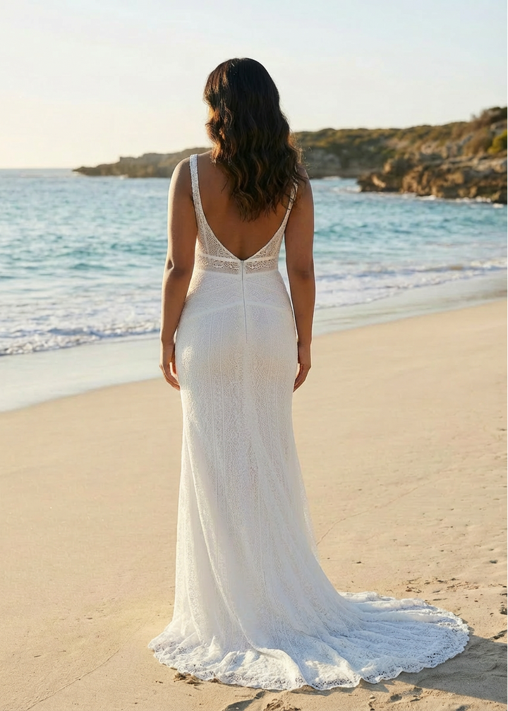 Woman in a lace wedding dress with a low back, standing on a beach with ocean and sky in the background.
