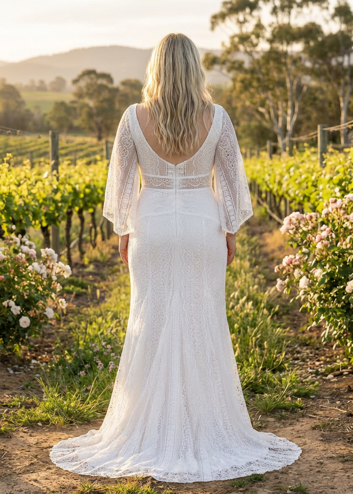 Woman in a lace column wedding dress standing in a vineyard at sunset