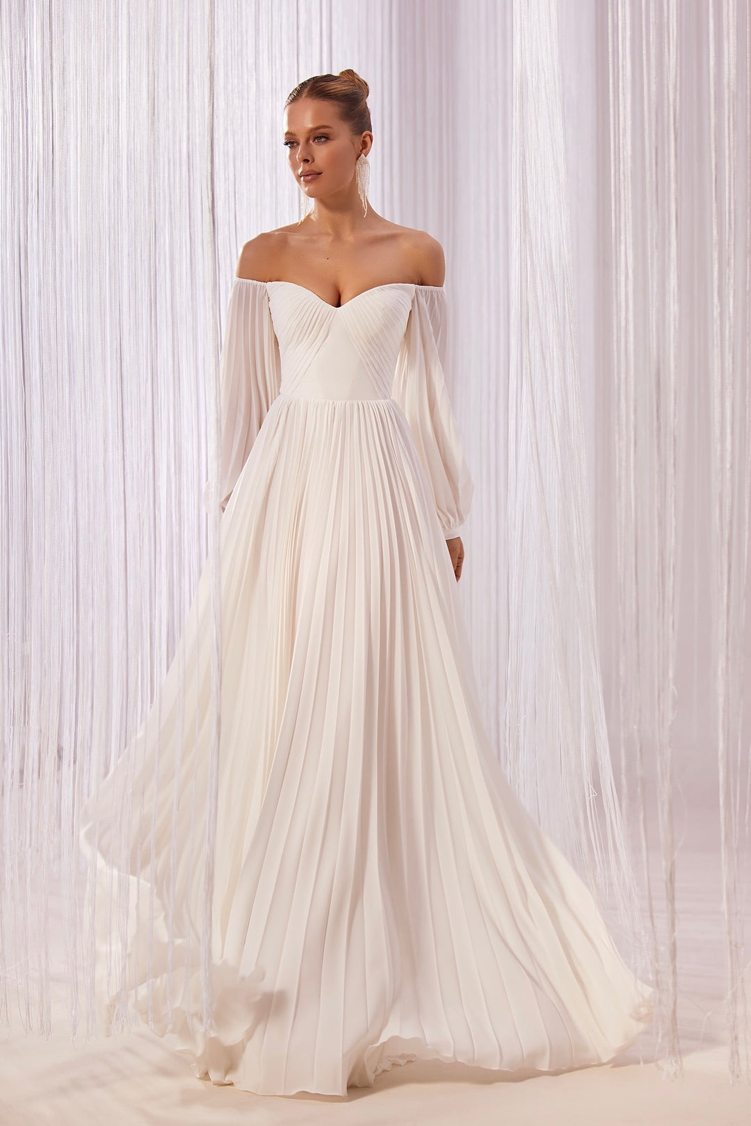 A woman models an off-the-shoulder, A-line chiffon wedding dress with pleats and a flowing skirt.