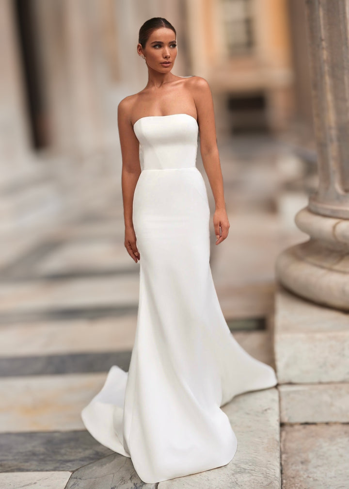 Woman wearing a strapless satin mermaid gown standing on stone steps.