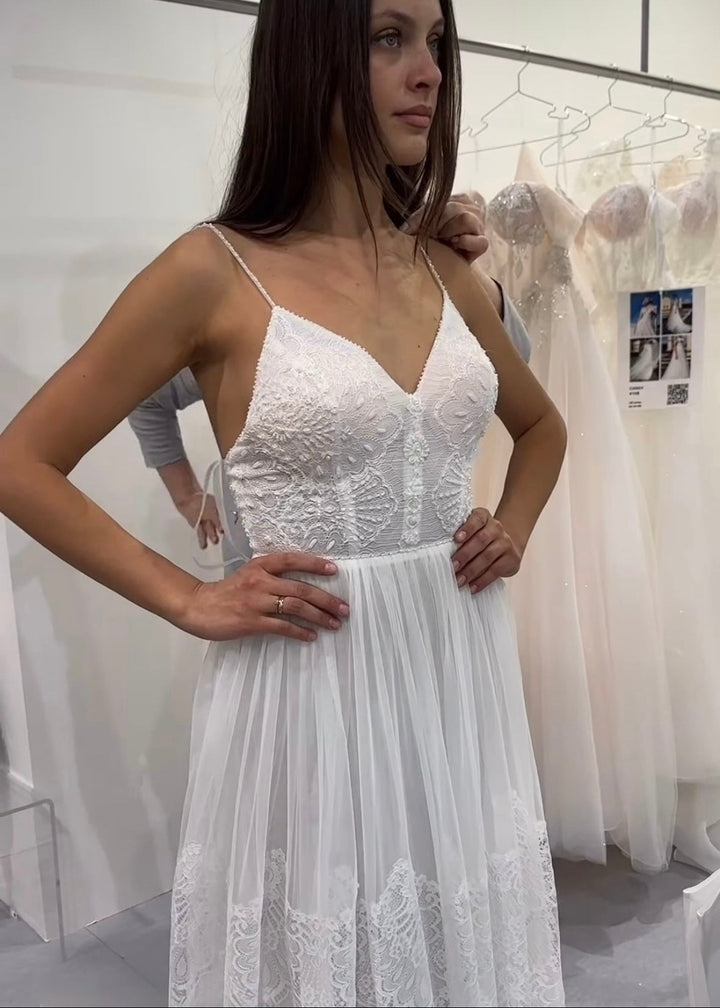 Woman in an a-line spaghetti strap lace and tulle wedding dress standing in a bridal showroom in front of a rack of dresses.