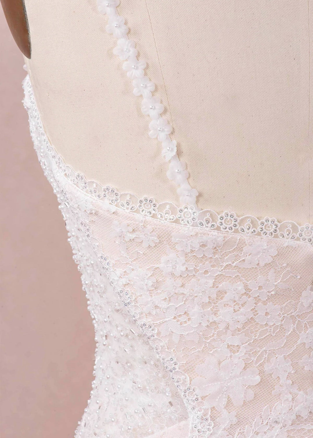 A close up of the back of a beaded and lace wedding dress with flower decorated spaghetti straps.