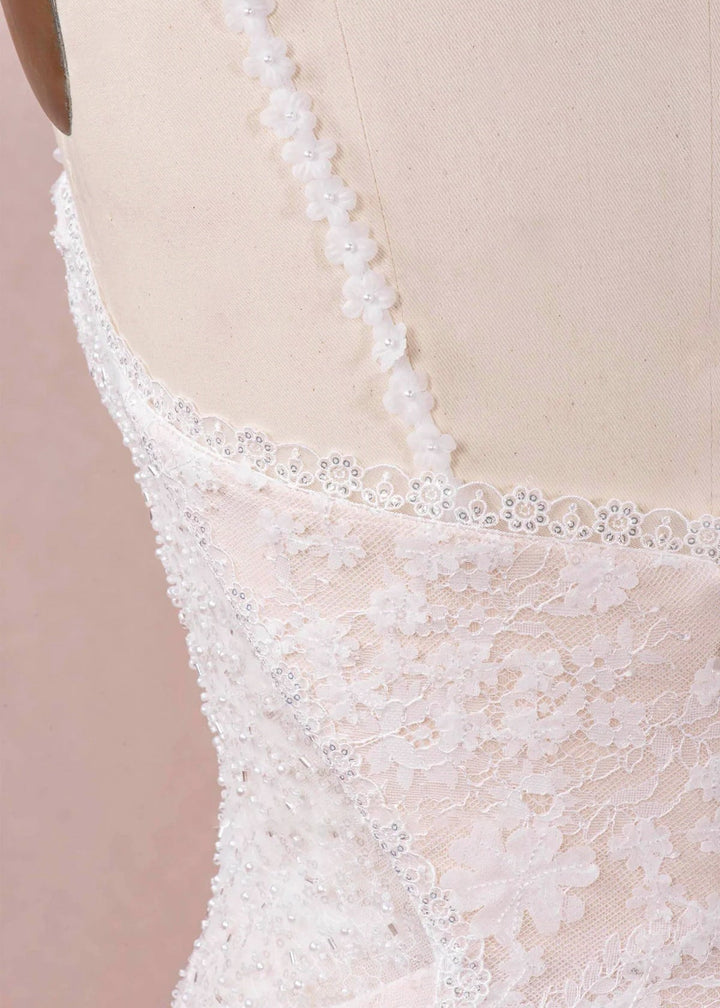 A close up of the back of a beaded and lace wedding dress with flower decorated spaghetti straps.