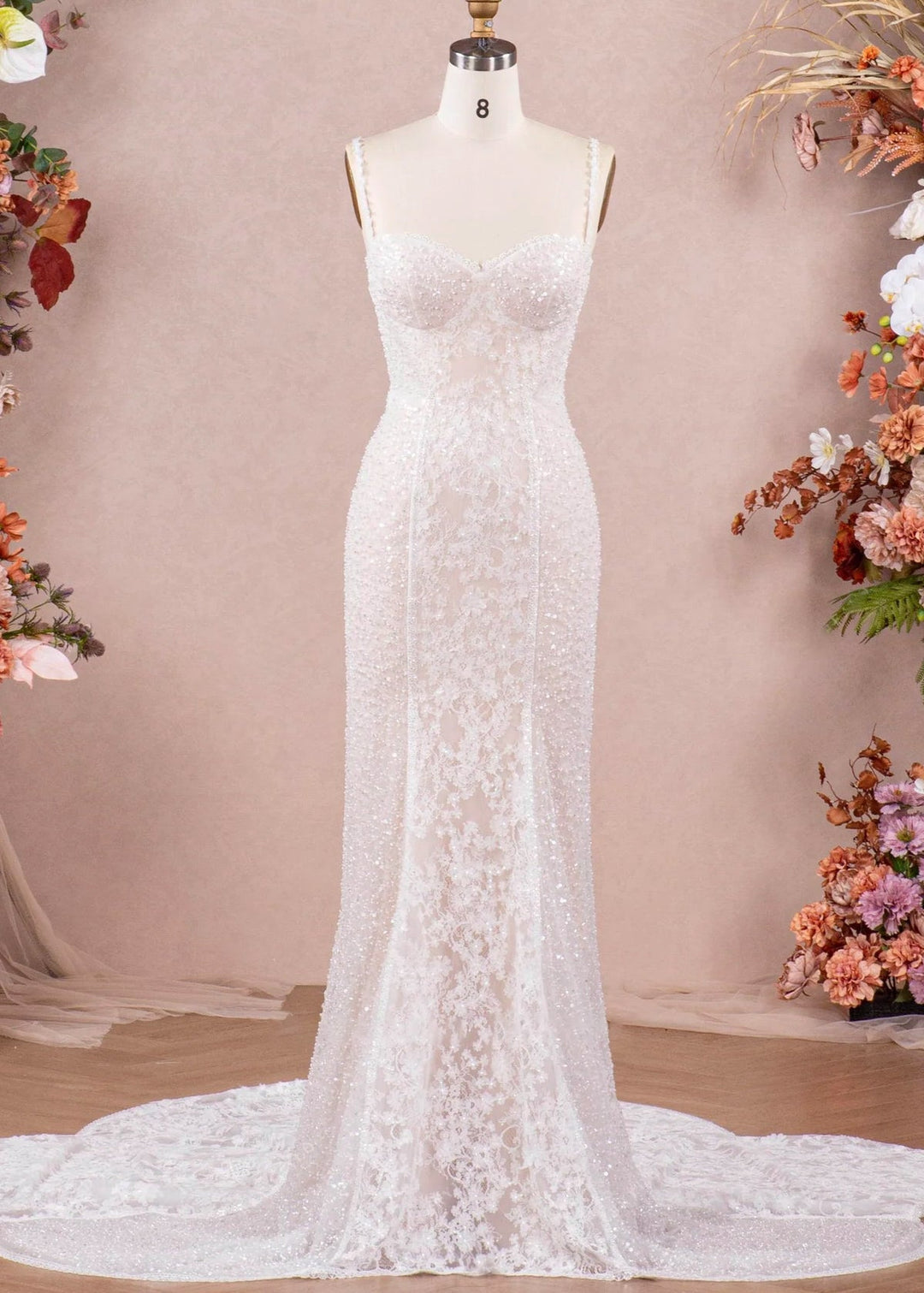 A fitted wedding dress with spaghetti straps, beading and lace on a mannequin in front of a studio setting.