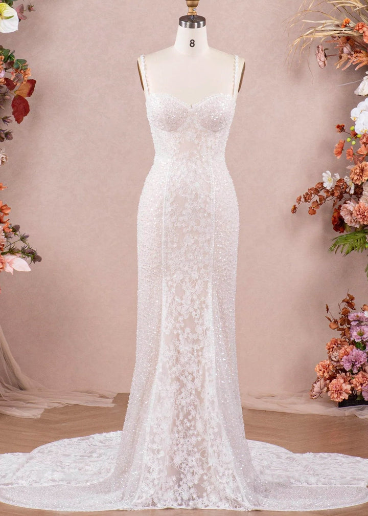 A fitted wedding dress with spaghetti straps, beading and lace on a mannequin in front of a studio setting.