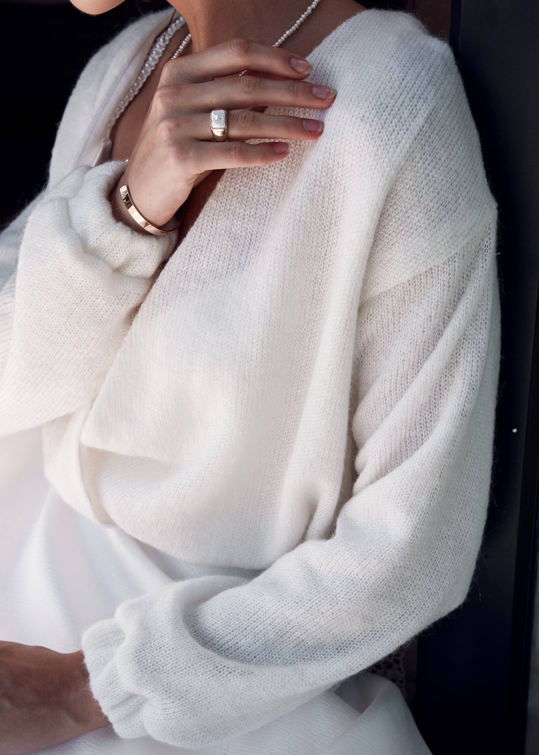 Close-up of a woman wearing a light ivory wool bridal cardigan with a blurred background.
