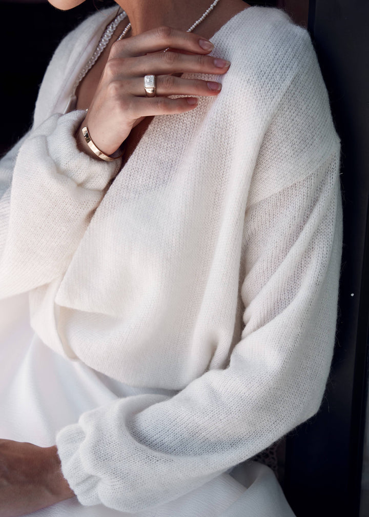 Close-up of a woman wearing a light ivory wool bridal cardigan with a blurred background.