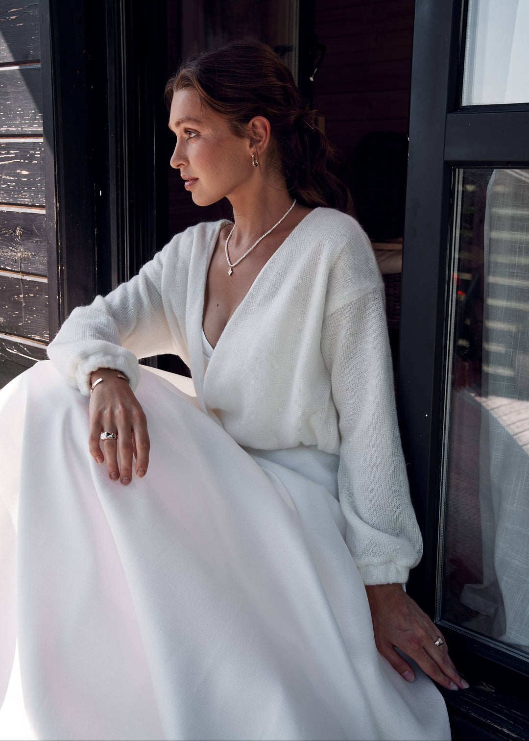 Woman in a white bridal dress sitting by a window with a cityscape view.