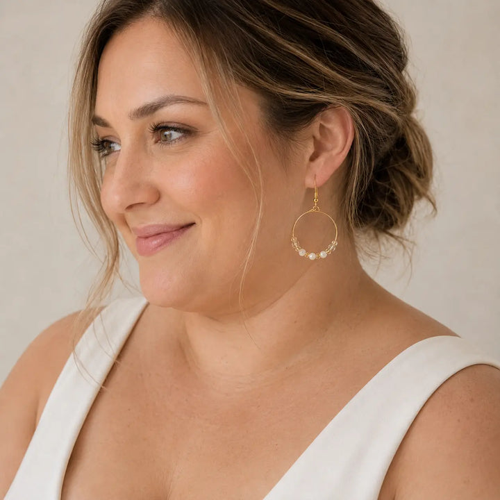 A woman wearing a delicate gold-plated hoop earring adorned with small white pearls and honey onyx beads shown in a close-up profile view against a soft beige background.