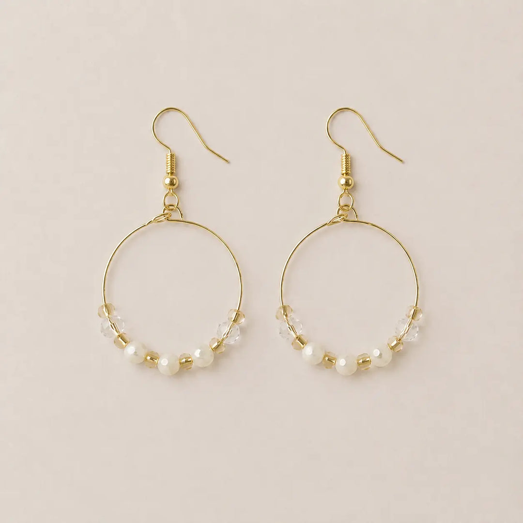 A pair of gold-plated hoop earrings with small freshwater pearls, clear faceted and honey onyx beads, displayed on a light beige background.