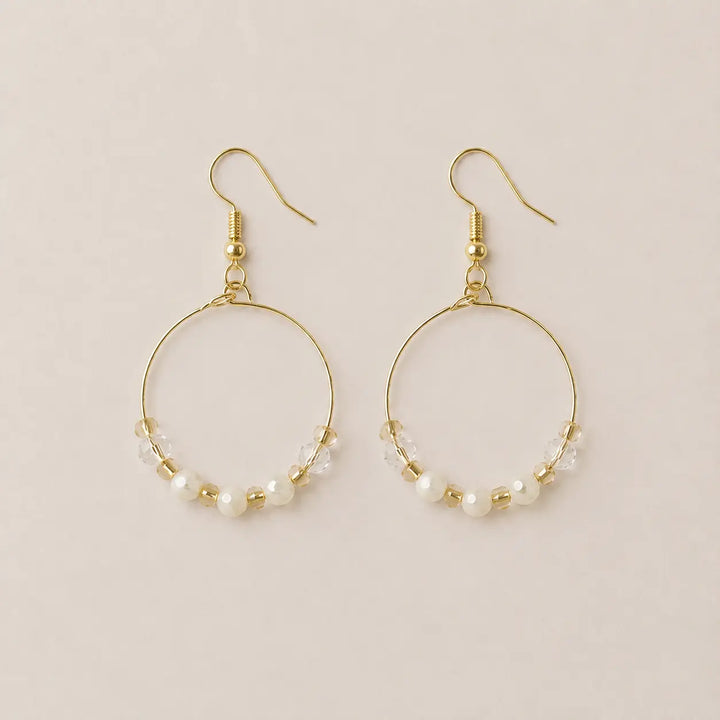 A pair of gold-plated hoop earrings with small freshwater pearls, clear faceted and honey onyx beads, displayed on a light beige background.