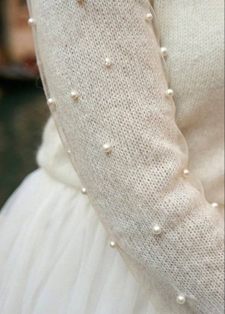 Close-up of a white wedding dress with pearl embellishments on the cardigan sleeves.