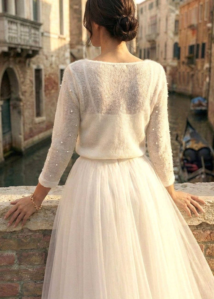 Woman in a white wedding dress with a wool cardigan standing by a canal in an Italian town.