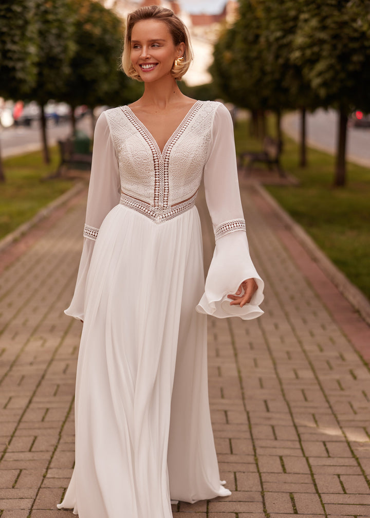 Woman in a white boho wedding dress with long sleeves standing on a brick path.
