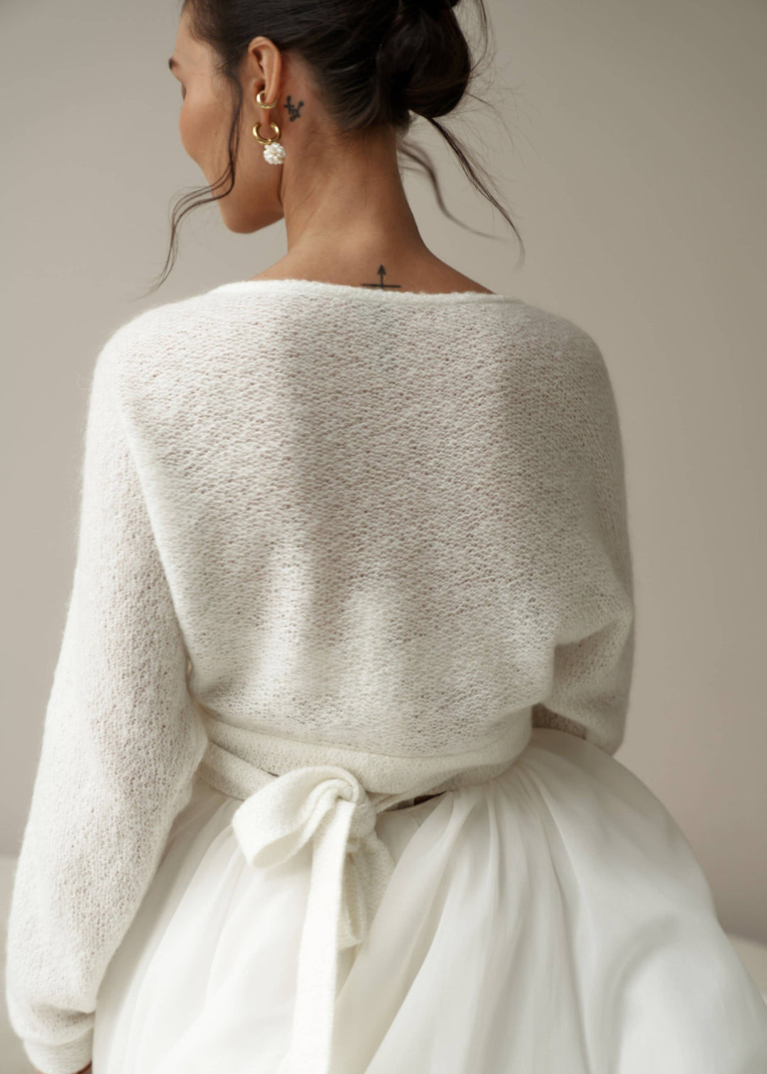 Woman wearing an ivory mohair cardigan over a white wedding dress against a neutral background