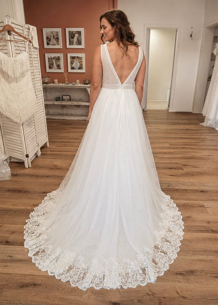 Woman wearing a white boho lace wedding dress standing in a bridal shop with her back to the camera showing the back of the dress.