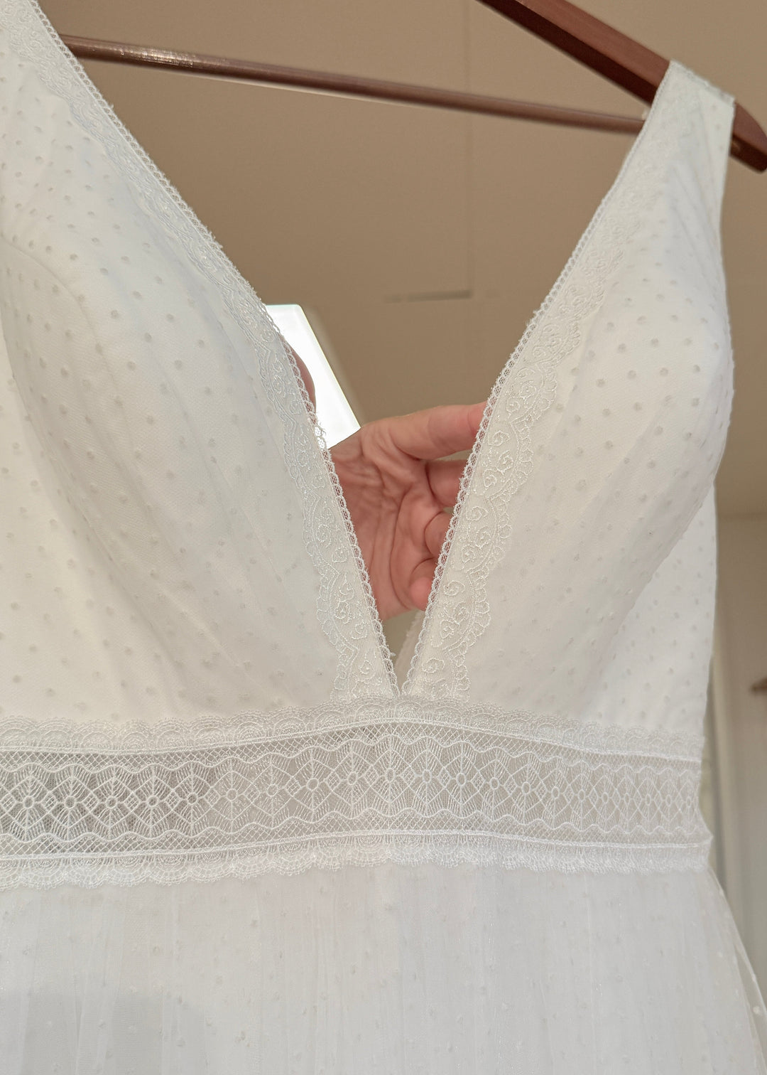 Close-up of a white swiss-dot lace wedding gown on a hanger with a neutral background.