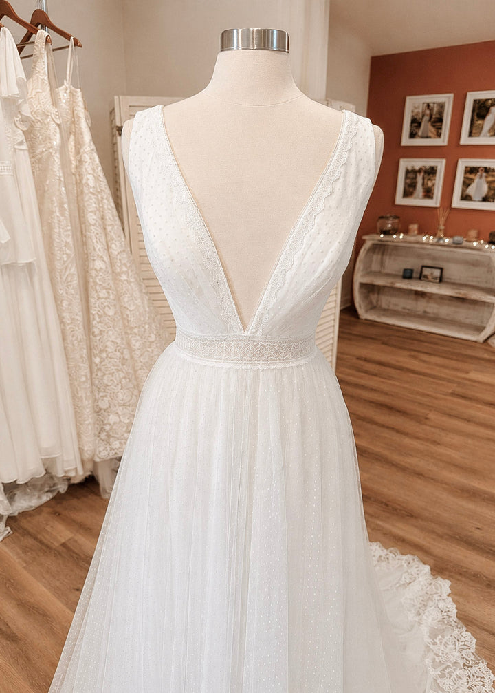 White boho lace wedding dress on a mannequin in a bridal store setting with other dresses in the background.