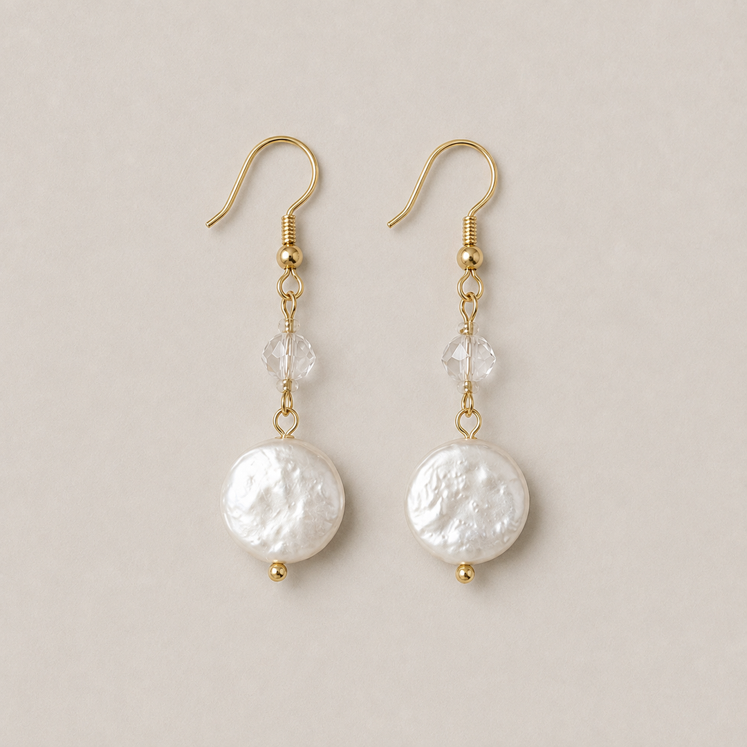 A pair of gold dangle earrings featuring textured freshwater pearls, clear faceted beads, and small gold beads, displayed on a neutral beige background.