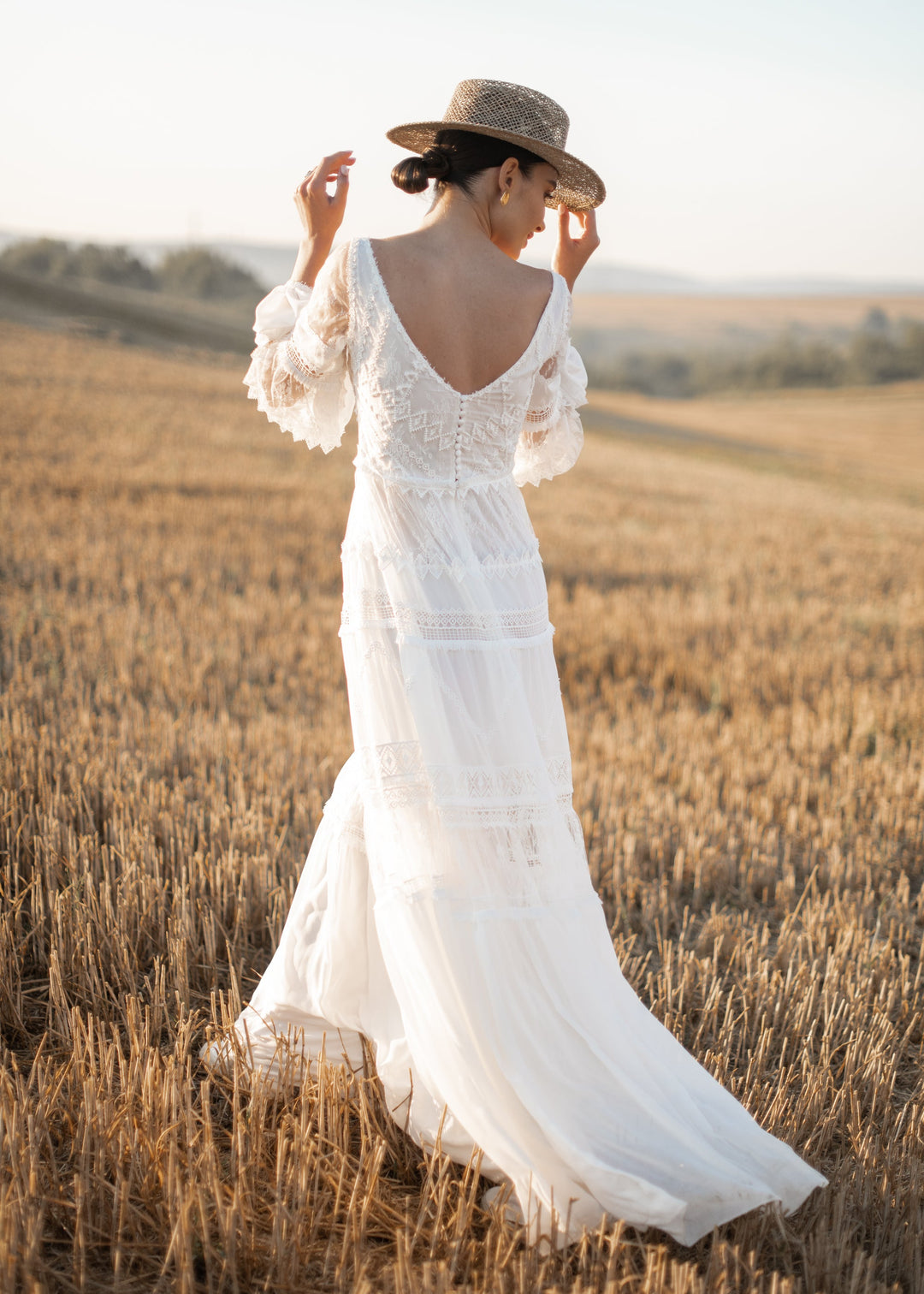 Woman in a boho wedding dress and straw hat standing in a wheat field.