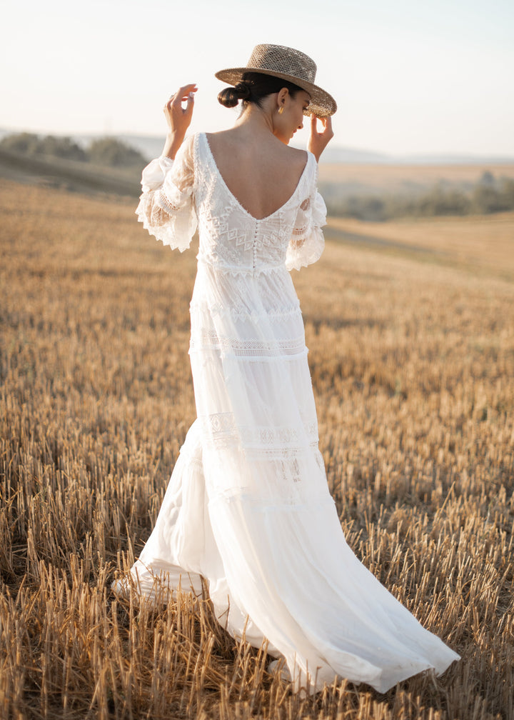 Woman in a boho wedding dress and straw hat standing in a wheat field.