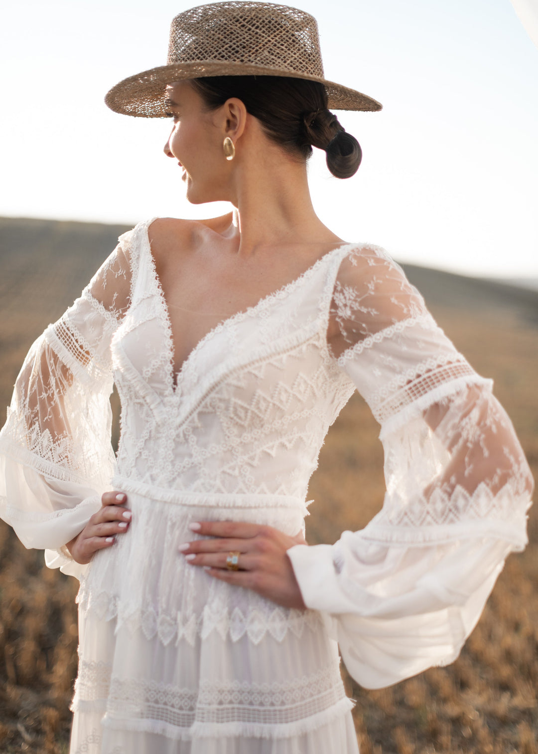 Woman wearing a boho lace wedding dress, Sisi by Nataliya Vilchuk, and straw hat against a blurred natural background
