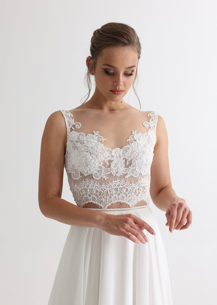 A woman wearing a white wedding dress with an illusion lace top and plain chiffon skirt standing against a white backdrop.