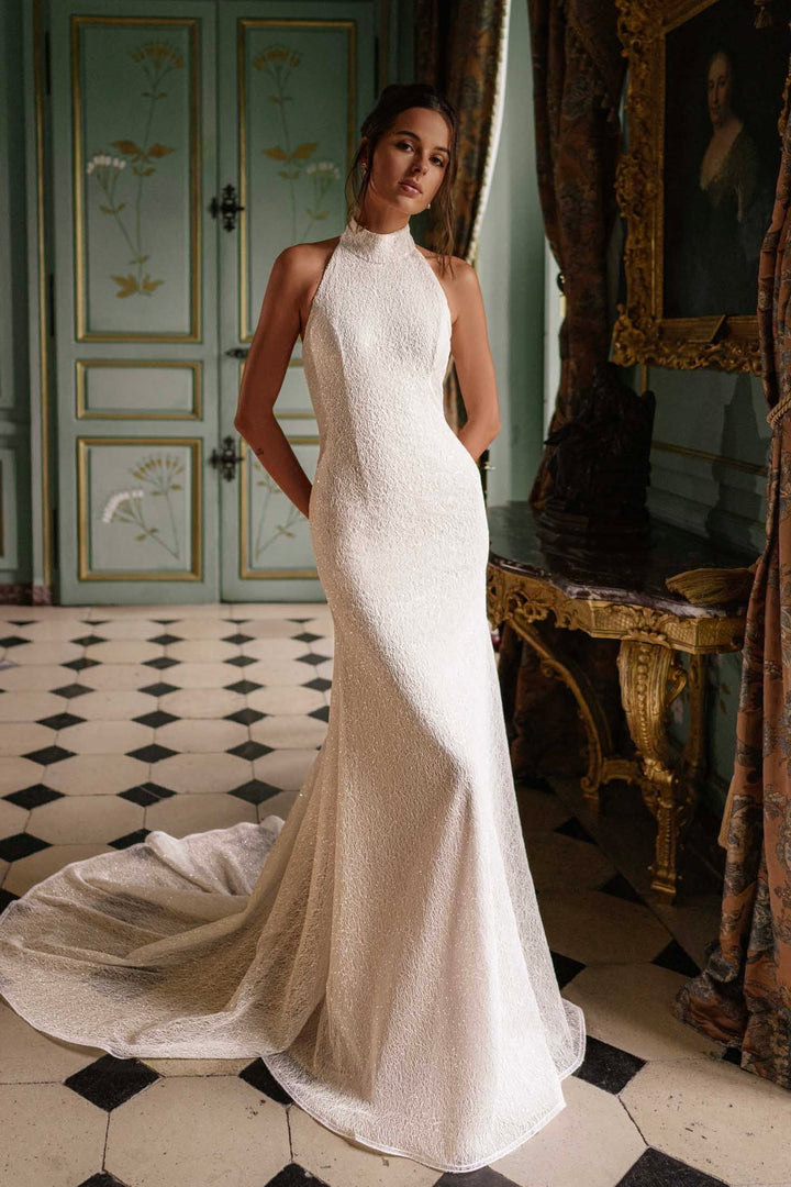 Video of a woman wearing a fitted wedding dress with a train, standing in a room.